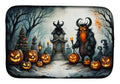 A rectangular mat with rounded corners featuring a detailed Halloween illustration. The design shows a dark, horned monster with a glowing orange beard holding a candle, standing in a spooky graveyard path with jack-o'-lantern pumpkins in the foreground, a haunted house, and bare trees in the background.