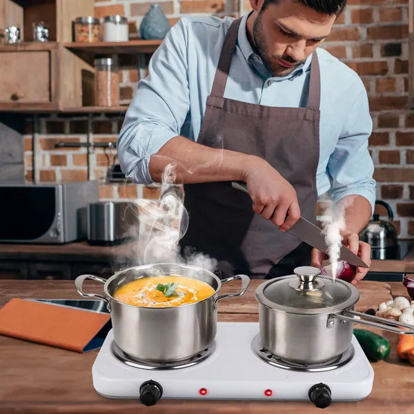 Man cooking in a kitchen with two pots on a hot plate.