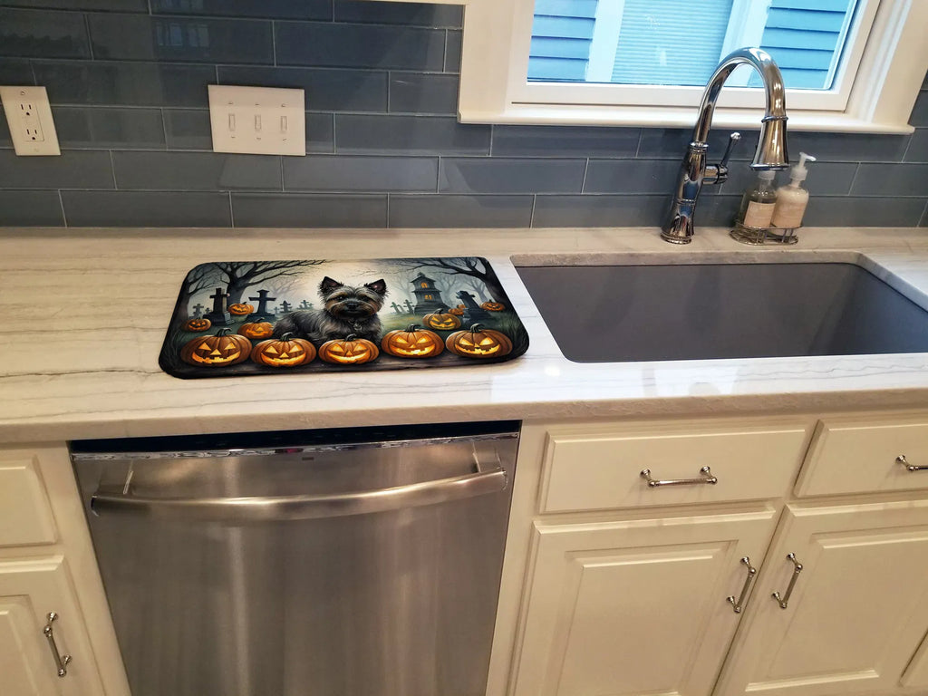 Halloween-themed mat with a cat and pumpkins on a kitchen counter next to a sink.